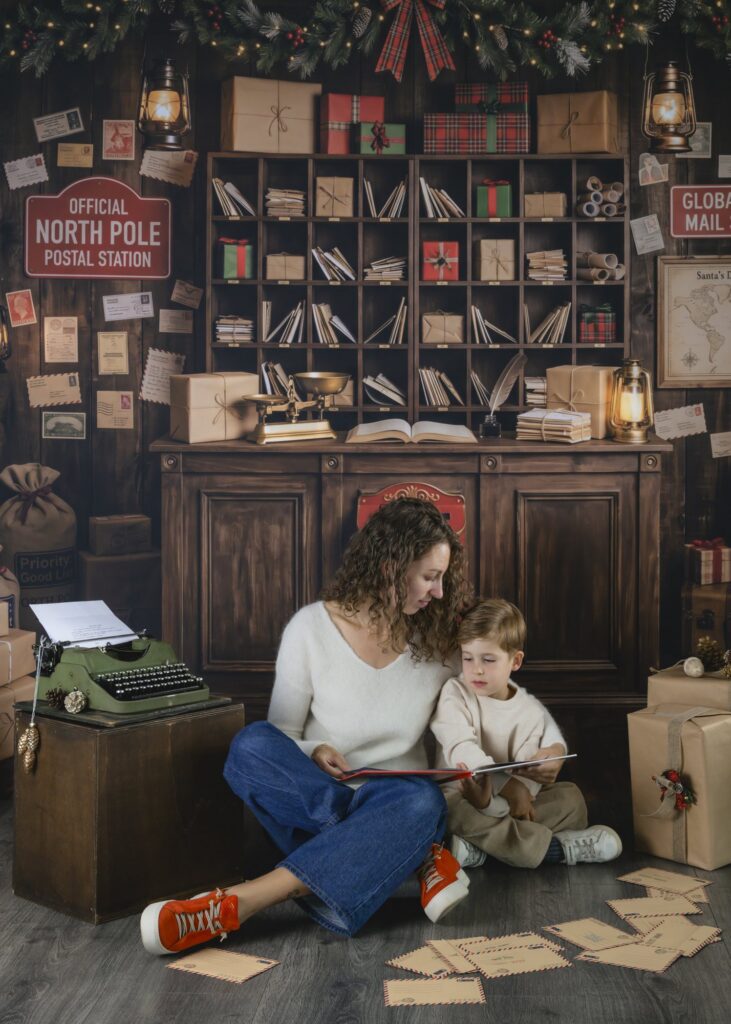 Un parent et son enfant lisant ensemble un livre de Noël, assis par terre dans le décor du bureau de poste, séance photo de Noël en famille à Haguenau